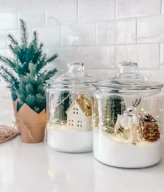 two glass jars filled with snow and christmas decorations