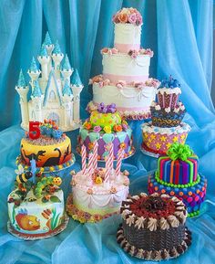 there are many different cakes on the table with blue fabric behind them and one has a castle