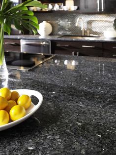 a bowl full of lemons sitting on top of a counter next to a vase filled with flowers