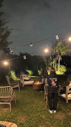 two people sitting on chairs in the grass at night with string lights strung above them