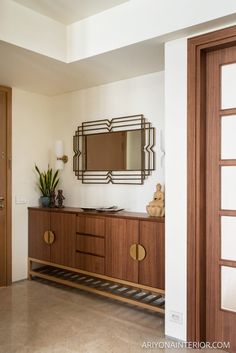 a large mirror on the wall above a wooden cabinet with two vases and a potted plant