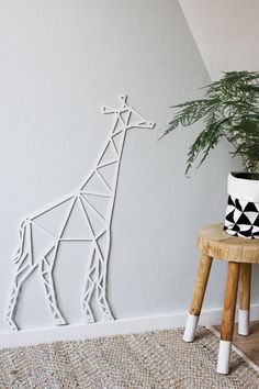 a giraffe cut out of paper sitting on top of a wooden stool next to a potted plant