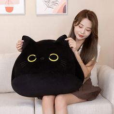 a woman sitting on a couch holding a black cat pillow