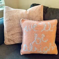 two crocheted pillows sitting on top of a gray couch next to a window