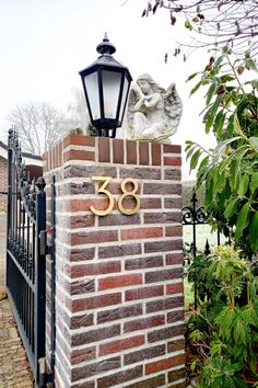 a brick wall with an iron gate and number sign on the top, next to a lamp post