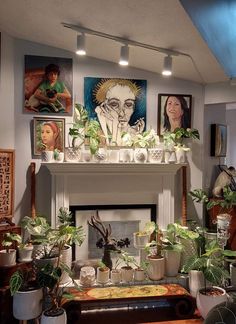 a living room filled with potted plants and pictures on the wall above it's fireplace