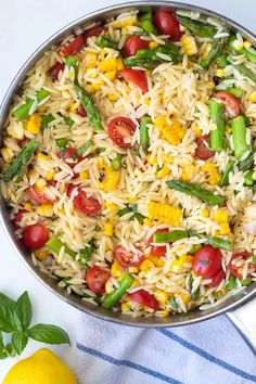 a pan filled with rice and vegetables on top of a table next to lemons