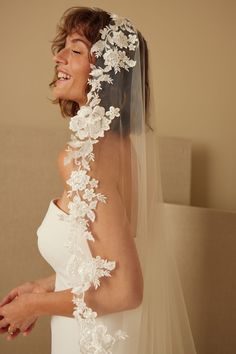 a woman wearing a wedding veil with flowers on the back of her head and shoulder