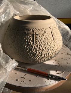 a clay pot sitting on top of a table next to a paintbrush and some plastic wrap