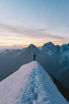 a person standing on top of a snow covered mountain with mountains in the background at sunset