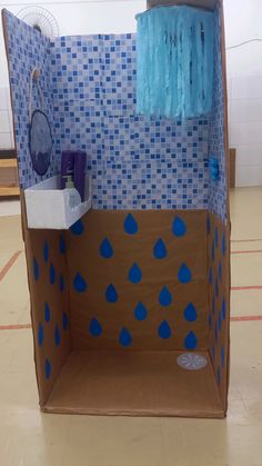 an open cardboard box with blue rain drops on the walls and inside it is a bathroom