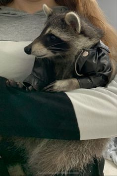 a woman holding a raccoon in her arms and wearing a leather jacket on it