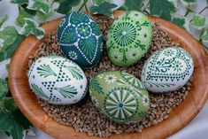 four decorated eggs sitting on top of a wooden bowl