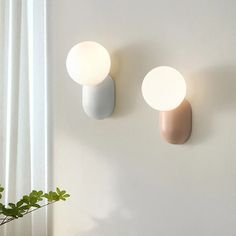 two wall lights mounted to the side of a white wall next to a potted plant