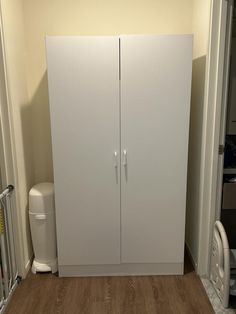 a tall white cabinet sitting in the corner of a room next to a trash can