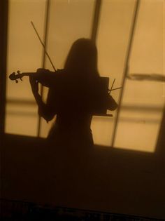 the silhouette of a woman playing violin in front of a window with long shadows on it