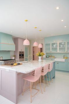 a kitchen with blue cabinets and pink chairs in front of an island countertop that has yellow lights hanging from the ceiling