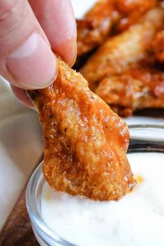 a person dipping something into a bowl of yogurt with chicken wings in the background