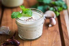 a glass jar filled with food sitting on top of a wooden table next to garlic and pepper