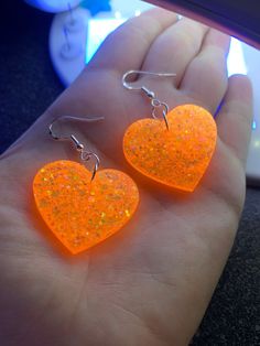 "Each pair of sparkly neon orange heart earrings are handmade to order, therefore no two pairs are identical! However, I try to get as close as possible :) Made with nickel-free & hypoallergenic sterling silver plated fishhook earrings. Hearts are approximately 1.25\", and are made with epoxy resin and neon orange holographic glitter! 🧡 UV blacklight reactive! Perfect for Halloween, concerts, raves, parties, festivals, etc.  Thanks for visiting my shop! ✨" Cute Orange Jewelry For Party, Cute Orange Party Jewelry, Fun Neon Earrings For Gifts, Heart-shaped Orange Jewelry For Gift, Orange Heart-shaped Jewelry Gift, Orange Heart Charm Jewelry, Fun Orange Jewelry For Gifts, Handmade Neon Jewelry For Gift, Handmade Orange Heart Jewelry