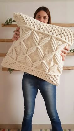 a woman holding up a white knitted pillow