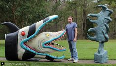 a man standing next to a statue of a fish with its mouth open and teeth out