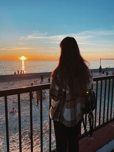 a woman looking out over the beach at sunset