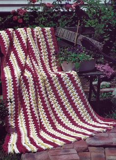 a crocheted blanket sitting on top of a brick walkway in front of flowers