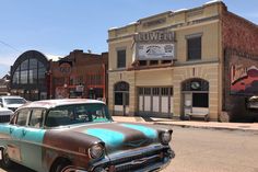 an old car parked in front of a building on the side of the road with other cars