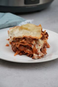 a piece of lasagna on a white plate next to an instant pressure cooker