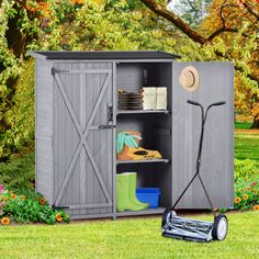 a garden shed with its door open and tools in the grass next to some flowers