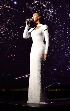 a woman standing on top of a stage wearing a white dress and holding a microphone