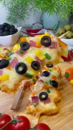 a pizza with olives, tomatoes and other toppings on a wooden cutting board