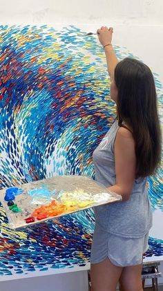 a woman is painting on the wall with colorful paint and brush in front of her