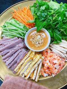 an assortment of vegetables and meats on a gold platter with dipping sauce in the center