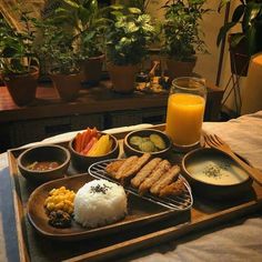 a tray with rice, carrots, and other foods on it next to a glass of orange juice