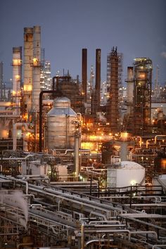 an oil refinery at night with lots of pipes in the foreground and buildings lit up behind it