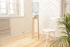 a white chair sitting next to a water bottle on top of a wooden stand in front of a window