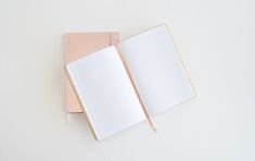 two notebooks sitting next to each other on top of a white table with a pink cover