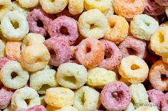 there are many different colored doughnuts in the pile on the table and one is pink, yellow, and white