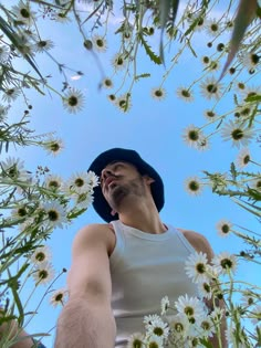 a man wearing a hat looking up into the sky with daisies in front of him