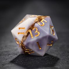 a white and gold dice with numbers on the side sitting on a black table top