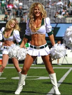 two cheerleaders in white and green outfits on the field at a football game