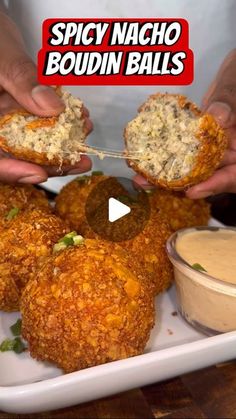 two hands holding up some food on a white plate with dipping sauce in the background