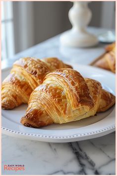 three croissants on a white plate sitting on a marble counter top next to other pastries