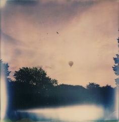 an old photo of a hot air balloon in the sky over a lake with trees