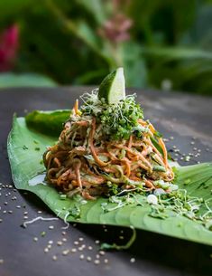 a green plate topped with noodles and veggies on top of a banana leaf