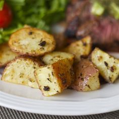 a white plate topped with potatoes and meat next to a pile of lettuce