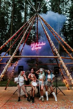 three women are posing for a photo in front of a tent with lights and confetti