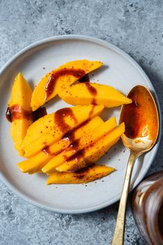 a white plate topped with sliced mangos next to a spoon and sauce on top of it